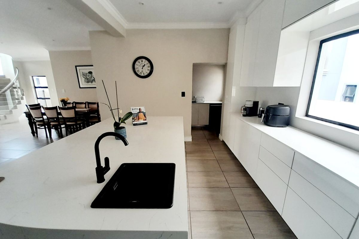 Modern kitchen featuring a large central island with quartz countertops, matte black fixtures, and sleek handleless cabinetry, seamlessly flowing into the dining area.