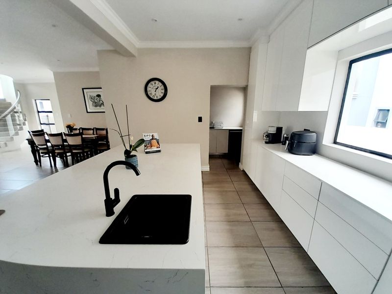 Modern kitchen featuring a large central island with quartz countertops, matte black fixtures, and sleek handleless cabinetry, seamlessly flowing into the dining area.