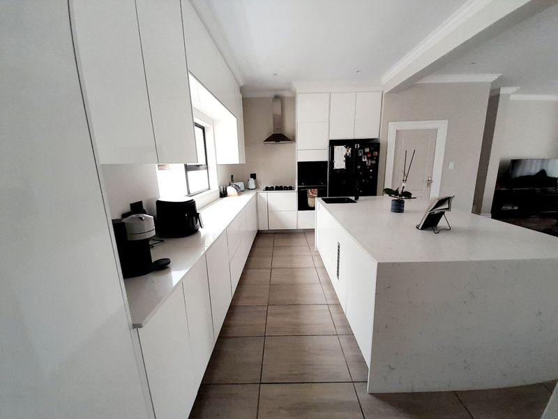 Modern kitchen featuring a large central island with quartz countertops, sleek white cabinetry, built-in oven, and high-quality tiled flooring.