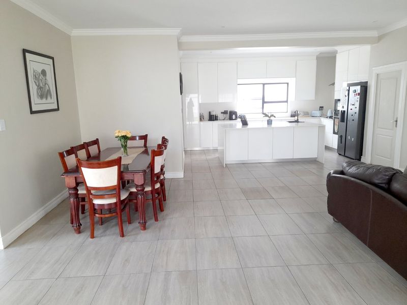 Spacious open-plan living and dining area featuring a modern kitchen with a central island, sleek cabinetry, and neutral tiled flooring throughout.