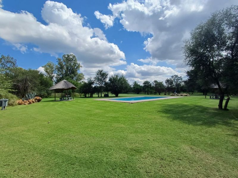 Expansive farm garden featuring a well-maintained swimming pool and a traditional thatched lapa, perfect for outdoor relaxation and entertainment.