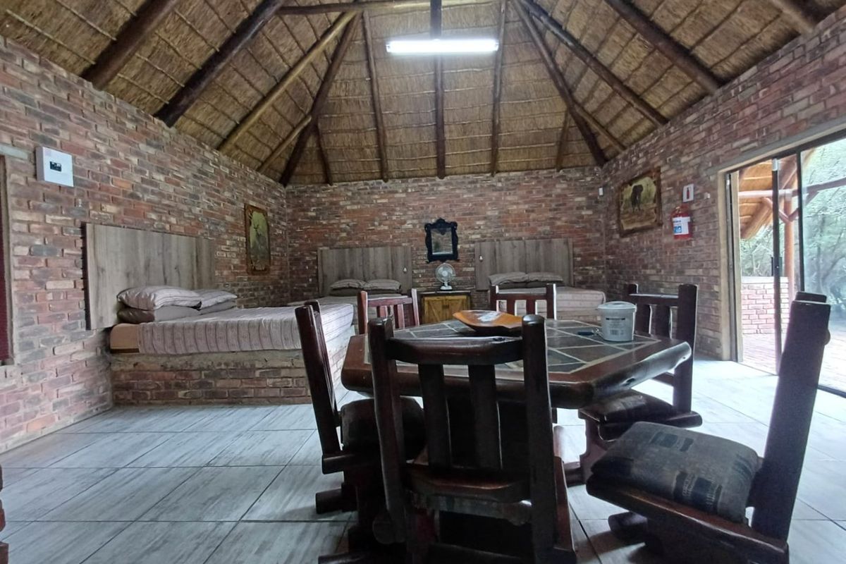 Spacious bedroom featuring a high thatched ceiling, exposed brick walls, built-in brick bed bases, and direct access to the outdoors via a sliding glass door.