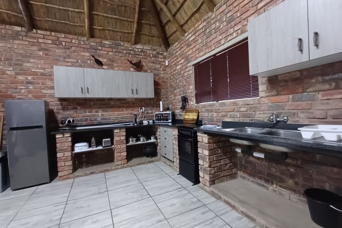 Rustic kitchen featuring exposed brick walls, a high thatched ceiling, granite countertops, and built-in brick cabinetry with tiled flooring.