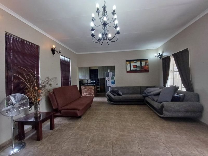 Spacious open-plan living area featuring ceramic floor tiles, a decorative chandelier, and a view through to the kitchen with a brick-base island.