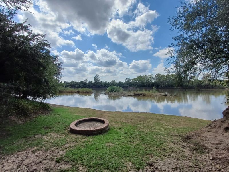 A scenic view of the riverfront area featuring a built-in brick fire pit set within a natural, grassy landscape.