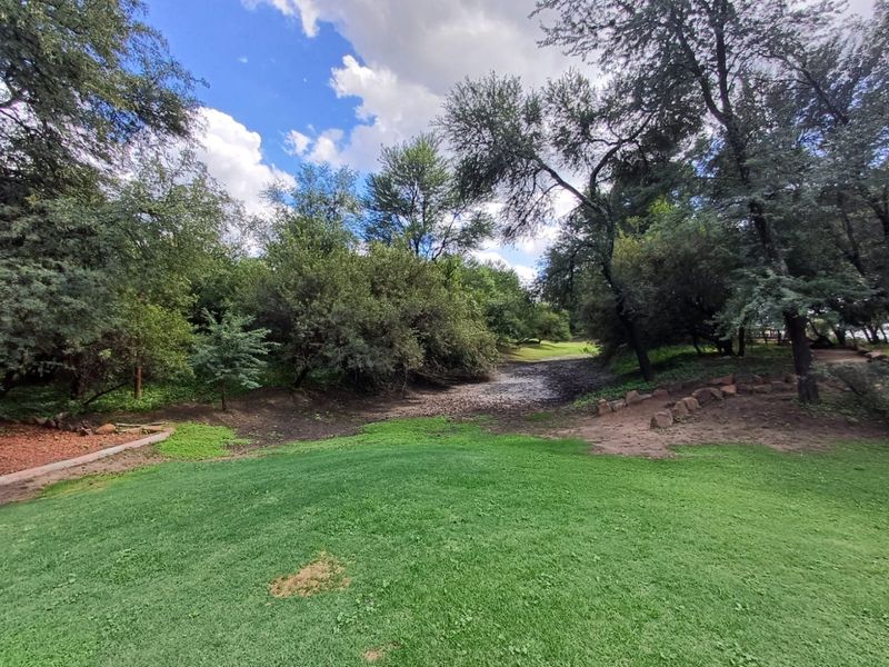 A well-maintained garden area featuring a lush green lawn, mature trees, and natural stone landscaping elements.