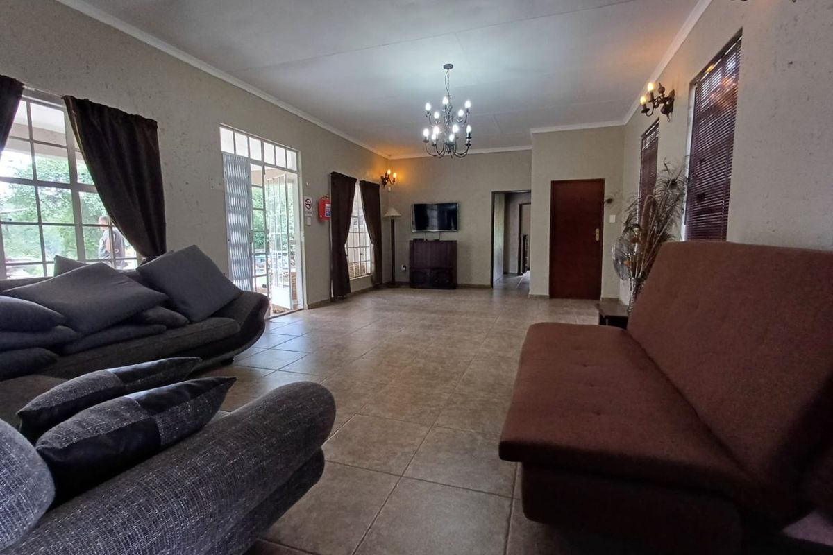 Spacious living room featuring tiled flooring, a central chandelier, and direct access to the exterior through a security gate.