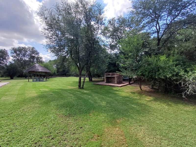 Spacious farm garden featuring a thatched lapa, a brick built-in braai area, and well-maintained lawn surrounded by mature trees.