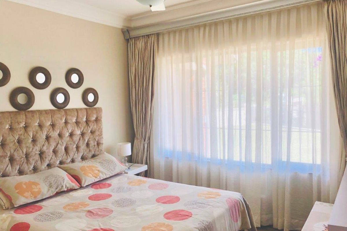 A well-lit bedroom featuring neutral wall tones, coving, and large windows dressed with floor-to-ceiling curtains.