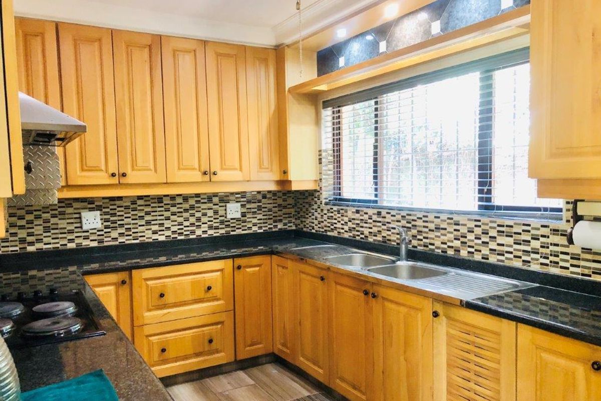 A functional kitchen featuring wooden cabinetry, granite countertops, a mosaic tile backsplash, and a stainless steel double sink with integrated hob and extractor.