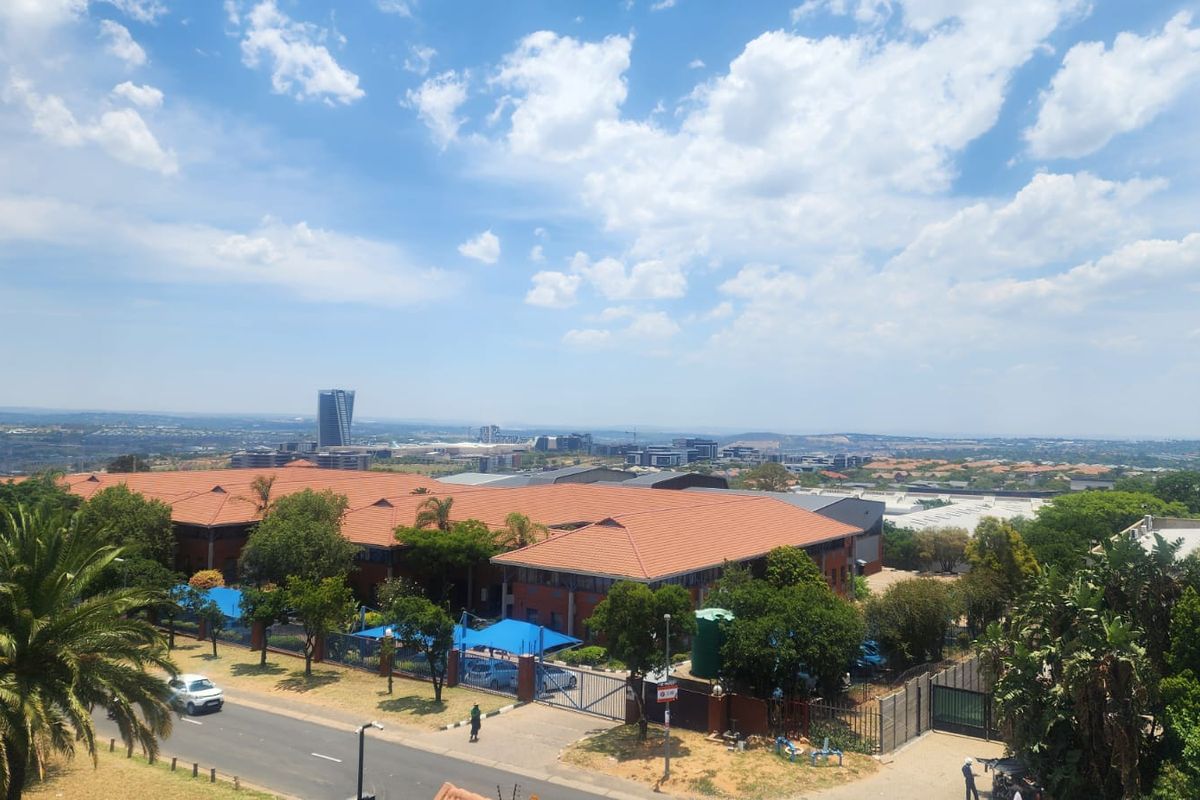 An elevated aerial view of a commercial property complex featuring tiled roofing, secure perimeter fencing, and paved parking areas with shade structures.
