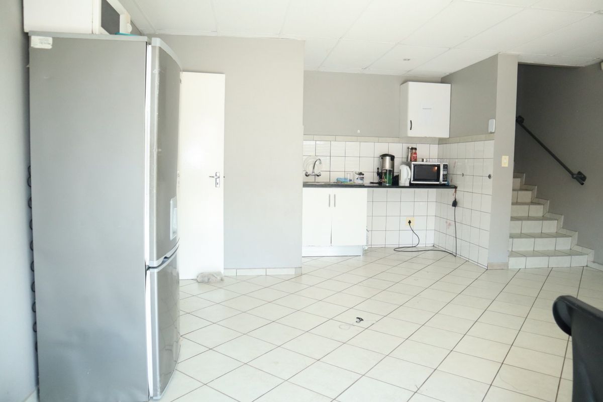 A functional kitchen area featuring tiled flooring, a tiled splashback, and built-in cabinetry, with an adjacent staircase leading to another level.