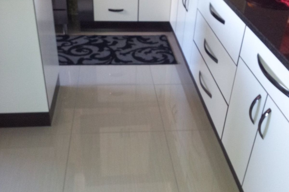A modern kitchen featuring white cabinetry, dark granite countertops, a gas stove, and polished tiled flooring with a mosaic tile backsplash.
