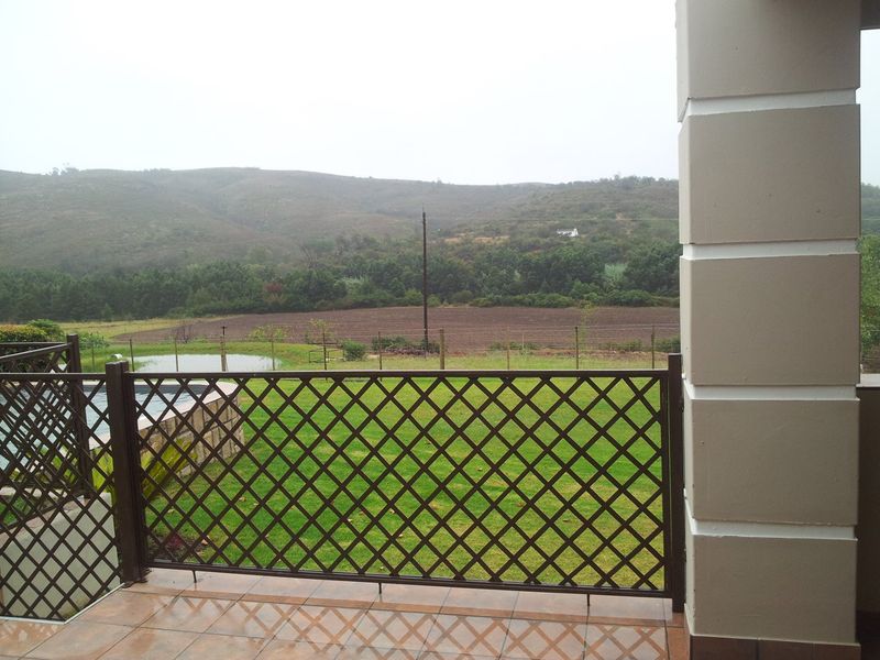 A covered patio area featuring tiled flooring and a lattice railing, offering scenic views of the surrounding farm landscape and garden.
