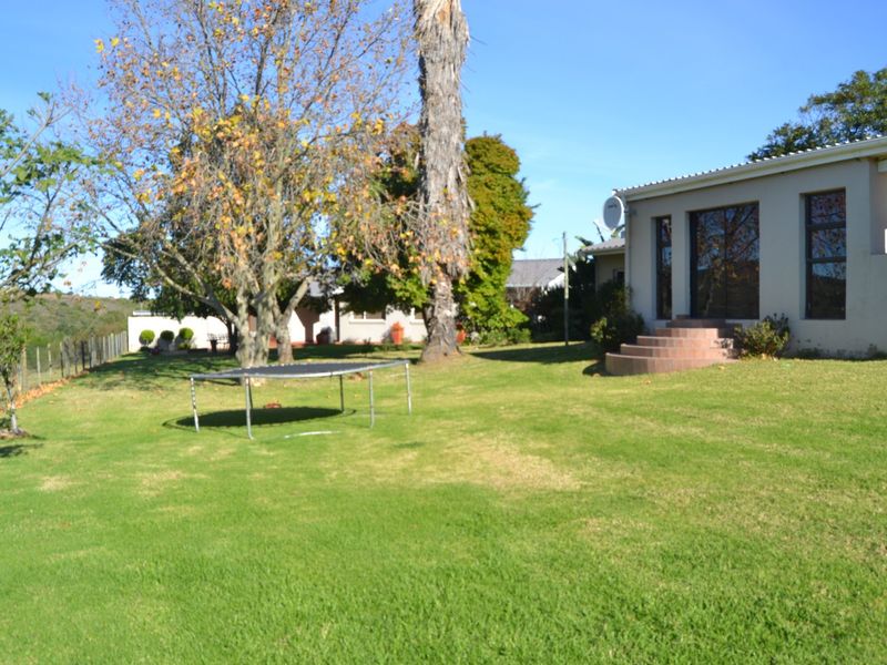 A spacious rear garden featuring a well-maintained lawn, mature trees, and a paved entrance with brick steps leading to the main dwelling.