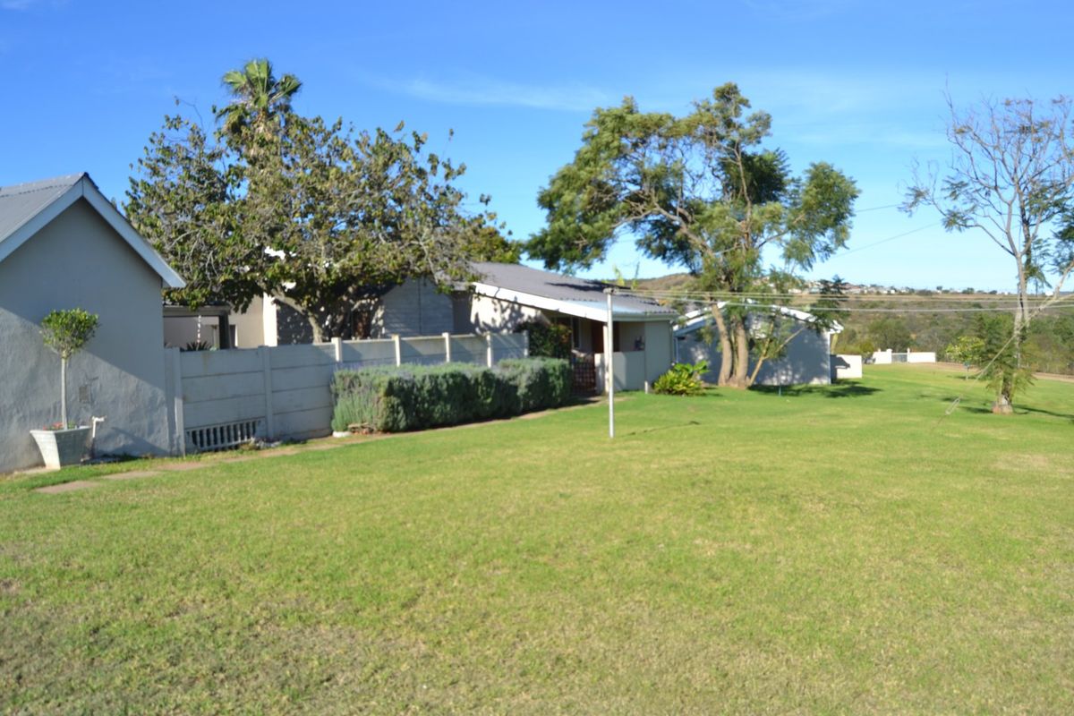 A view of the rear exterior of the farm property, featuring a large lawn, mature trees, and a precast concrete boundary wall.
