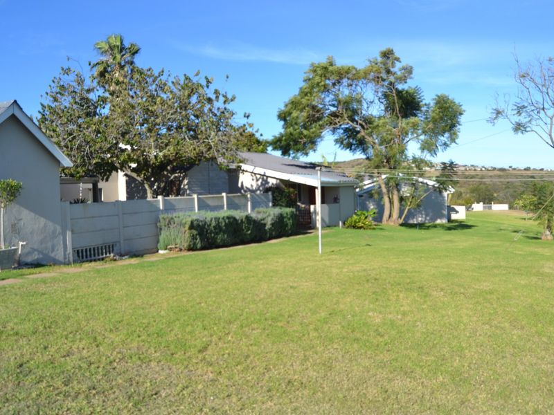 A view of the rear exterior of the farm property, featuring a large lawn, mature trees, and a precast concrete boundary wall.