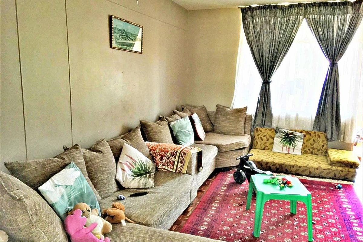 A living room featuring parquet flooring and large windows with curtain rails, offering a functional space with potential for cosmetic updates.