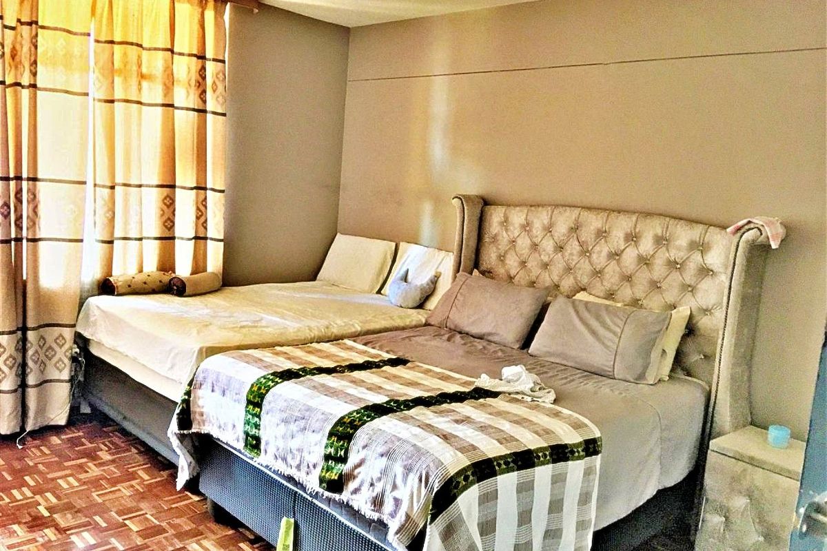 A bedroom featuring parquet flooring and large windows with curtains, providing a functional space for rest.