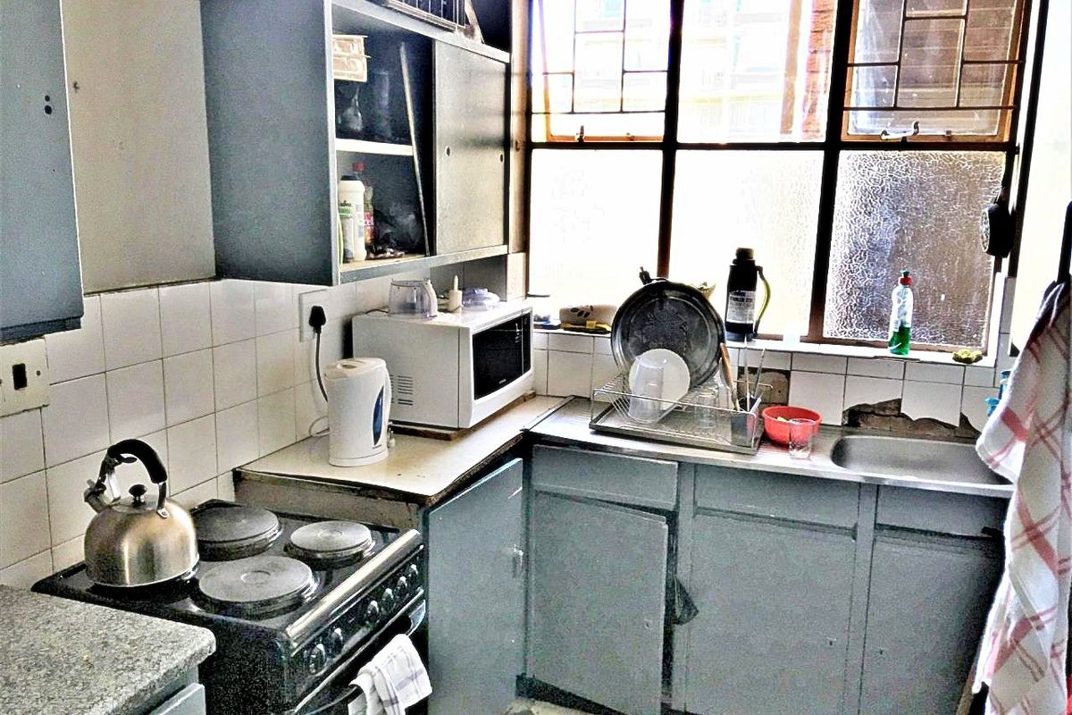 A dated kitchen featuring original cabinetry, a stainless steel sink, and tiled backsplash, requiring significant renovation to modernize the space.