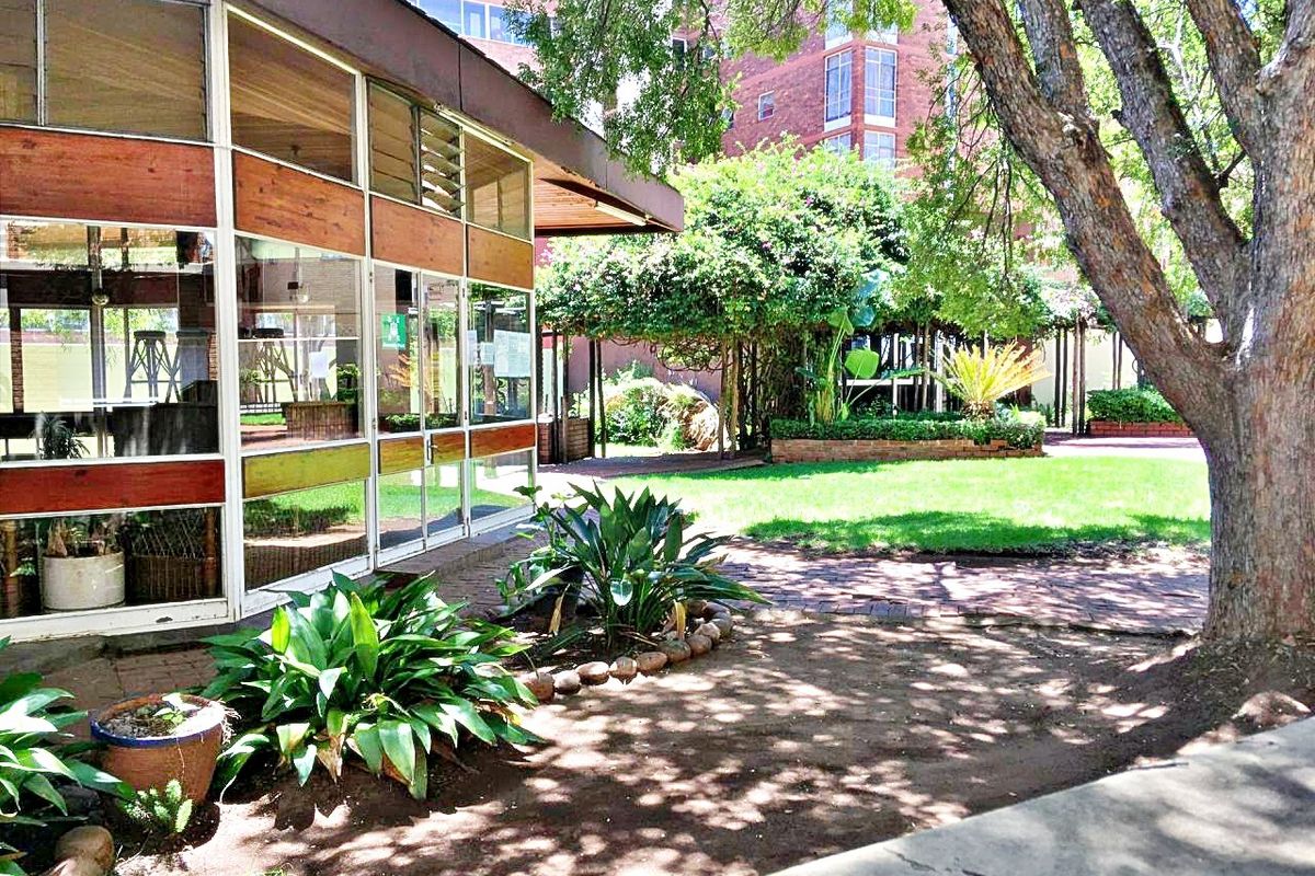 A view of the rear exterior featuring a large glass-walled structure, brick pathways, and a well-established garden with mature trees.