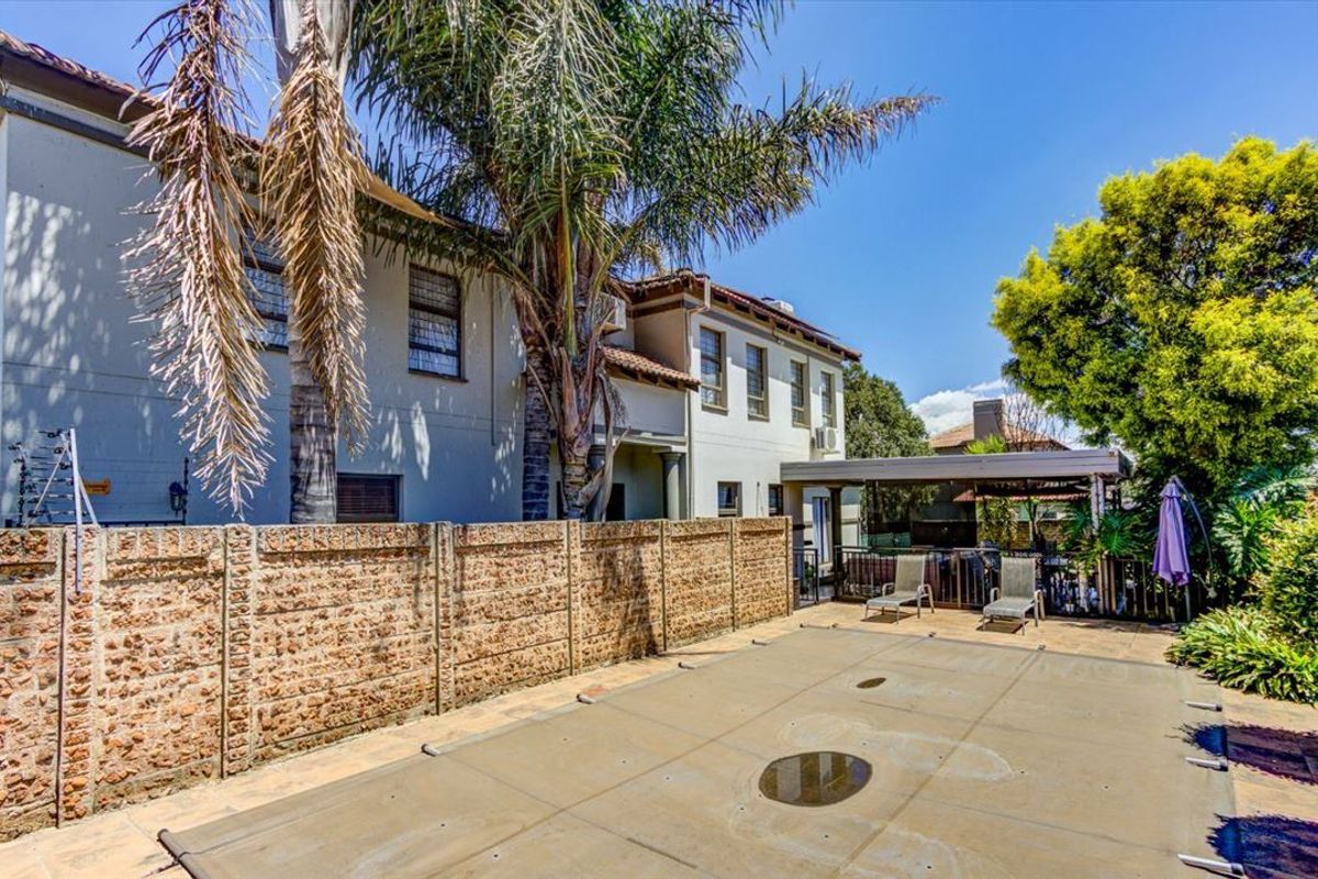Rear exterior view featuring a swimming pool with a cover, a precast concrete boundary wall, and a covered patio area.