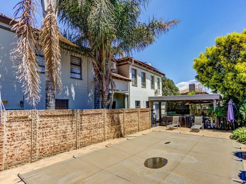 Rear exterior view featuring a swimming pool with a cover, a precast concrete boundary wall, and a covered patio area.