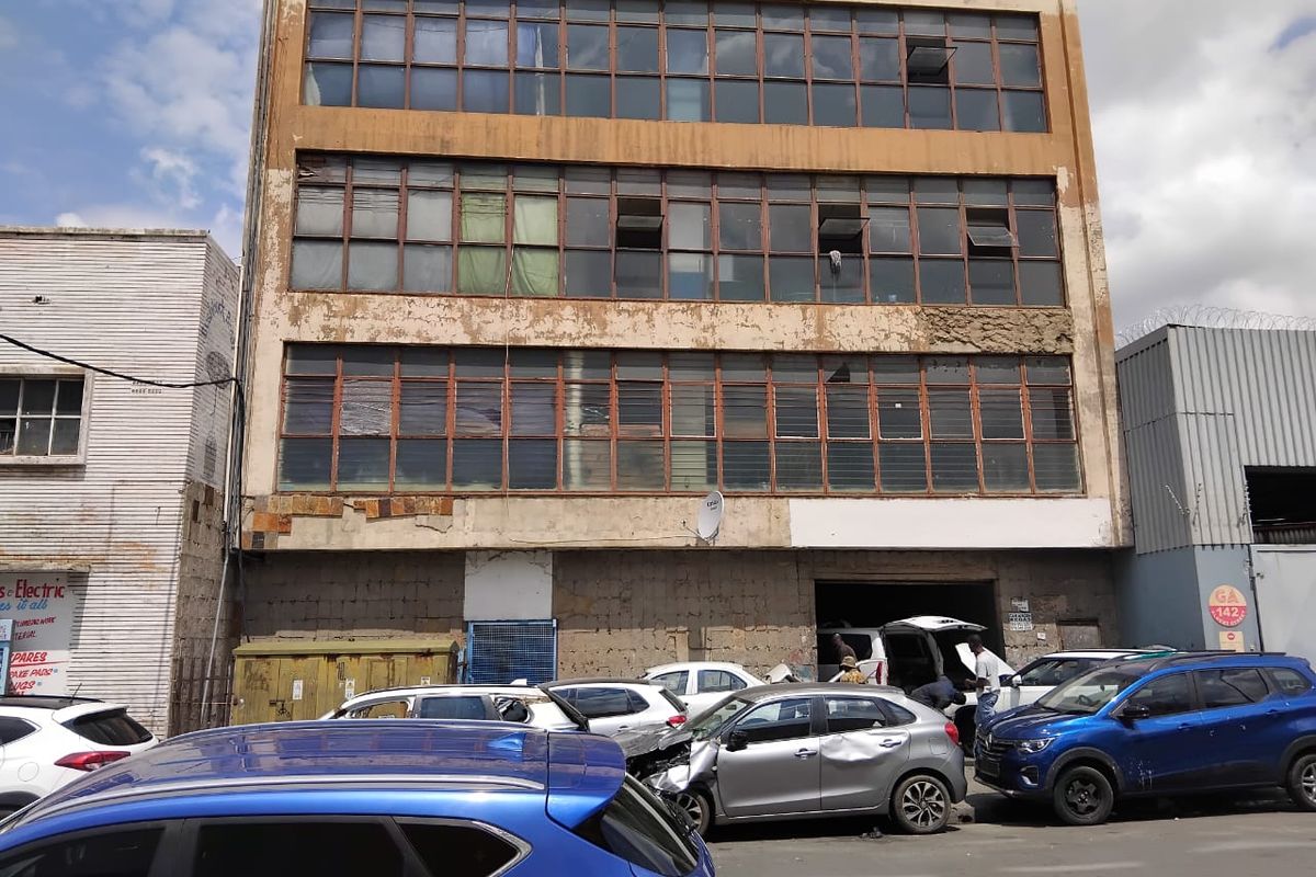 A multi-story commercial building facade featuring industrial metal-framed windows and ground-level access, showing significant signs of exterior wear and weathering.