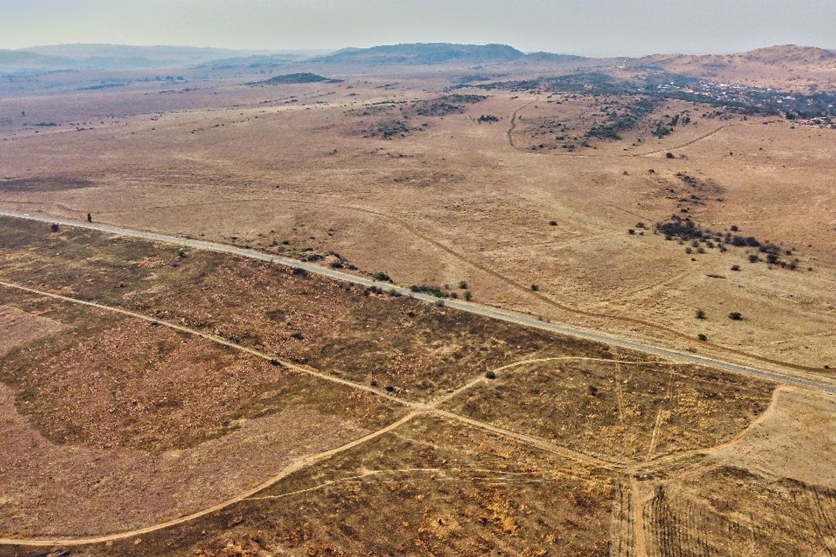 An aerial view of a large, undeveloped residential land parcel featuring natural terrain and adjacent road access.