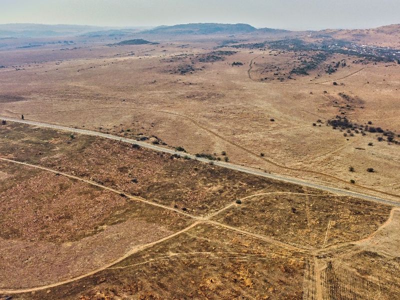 An aerial view of a large, undeveloped residential land parcel featuring natural terrain and adjacent road access.