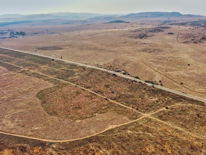 An aerial view of a large, undeveloped residential land parcel featuring natural terrain, dirt access tracks, and adjacent paved road frontage.