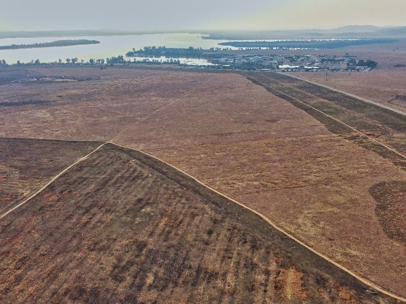 An aerial view of a large, vacant residential land parcel featuring natural terrain and distant water views.
