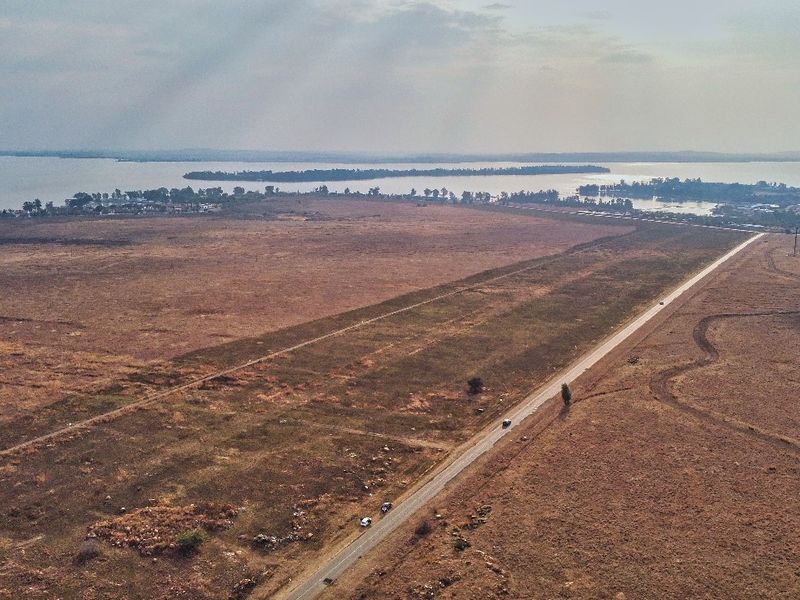Aerial view of a large, vacant residential land parcel featuring expansive open space and direct access to a paved road with distant water views.
