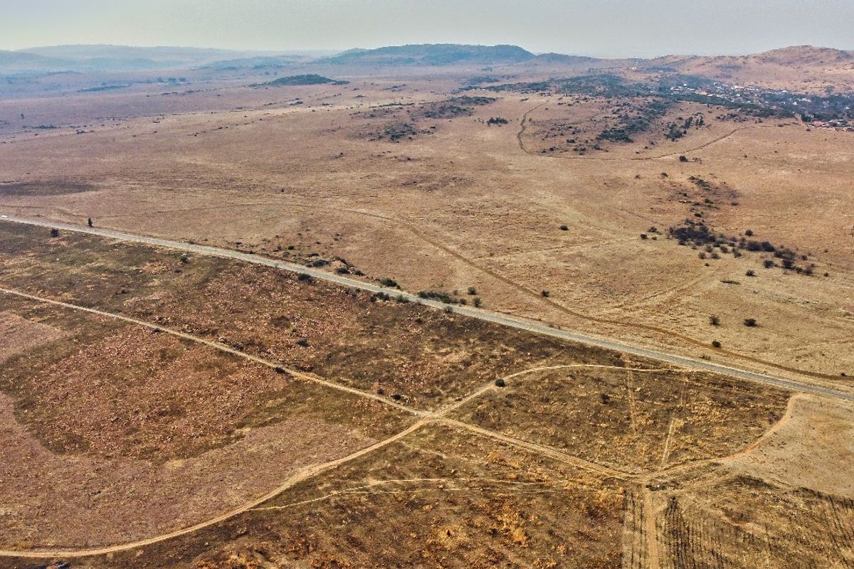 An aerial view of a large, undeveloped residential land parcel featuring natural terrain and direct access to a paved road.