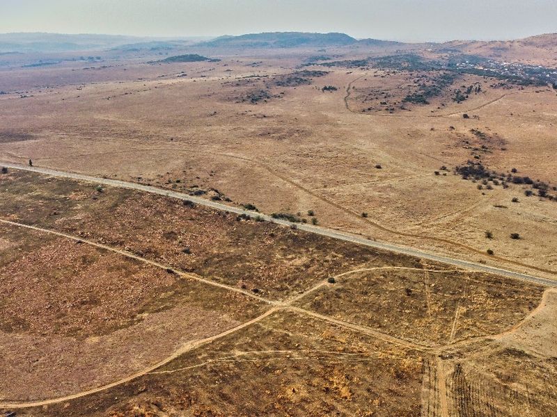 An aerial view of a large, undeveloped residential land parcel featuring natural terrain and direct access to a paved road.
