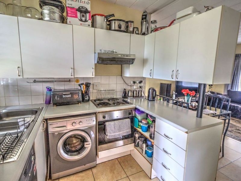 Compact kitchen featuring white cabinetry, laminate countertops, built-in oven and hob, and tiled flooring, with an integrated laundry appliance space.
