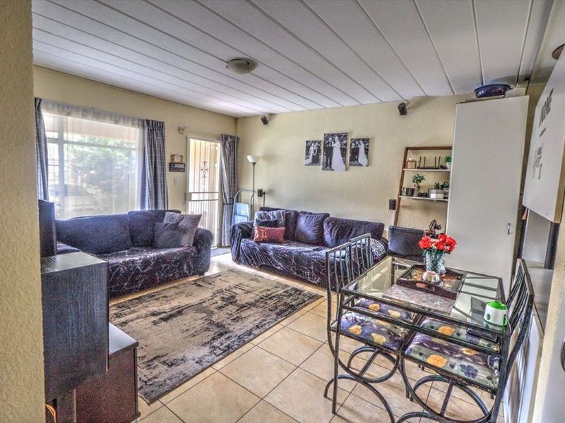 Open-plan living and dining area featuring tiled flooring, a panelled ceiling, and direct access to the exterior through a sliding glass door.