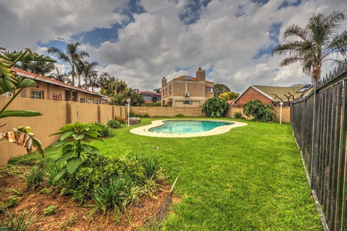 A well-maintained backyard featuring a swimming pool, lush green lawn, and secure perimeter fencing, providing a private outdoor space.