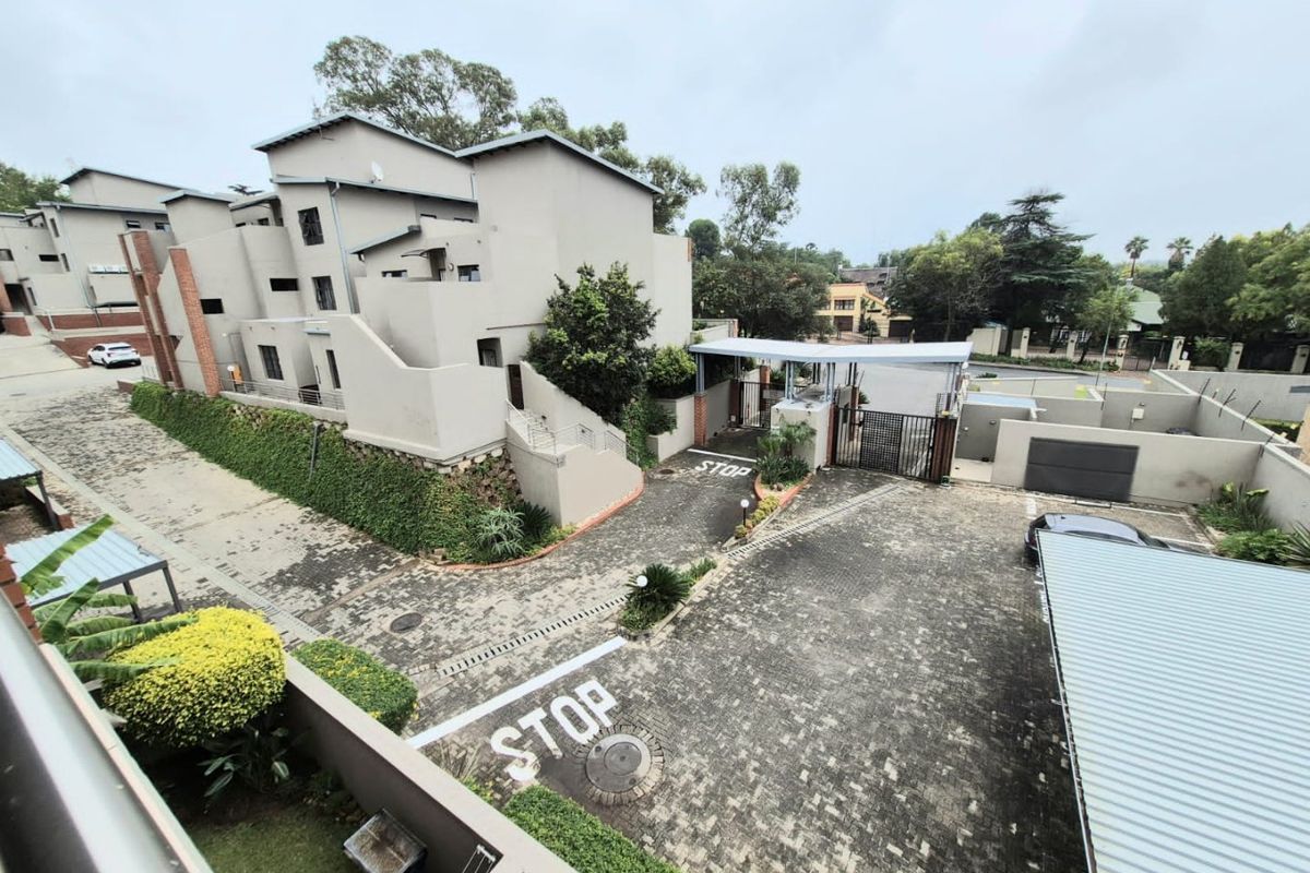 An elevated aerial view of the apartment complex entrance, featuring paved driveways, security access gates, covered parking, and well-maintained landscaped grounds.