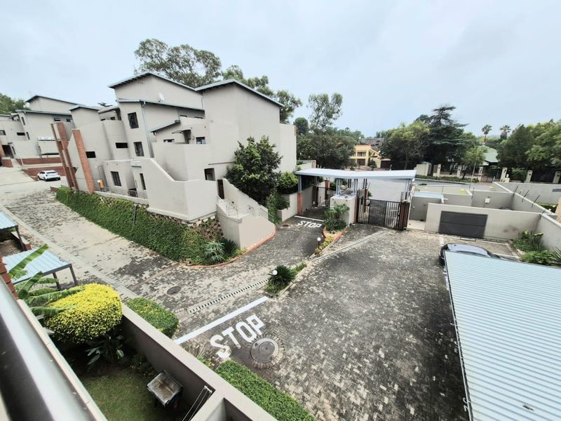 An elevated aerial view of the apartment complex entrance, featuring paved driveways, security access gates, covered parking, and well-maintained landscaped grounds.