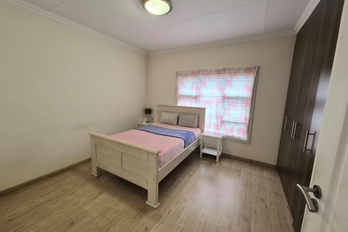 A well-maintained bedroom featuring light-toned laminate flooring, a built-in wardrobe, and a central ceiling light fixture.