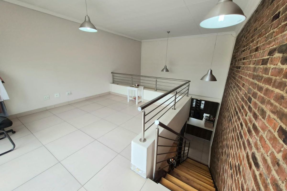 An open-plan mezzanine living area featuring an exposed brick wall, tiled flooring, and a modern stainless steel balustrade overlooking the staircase.