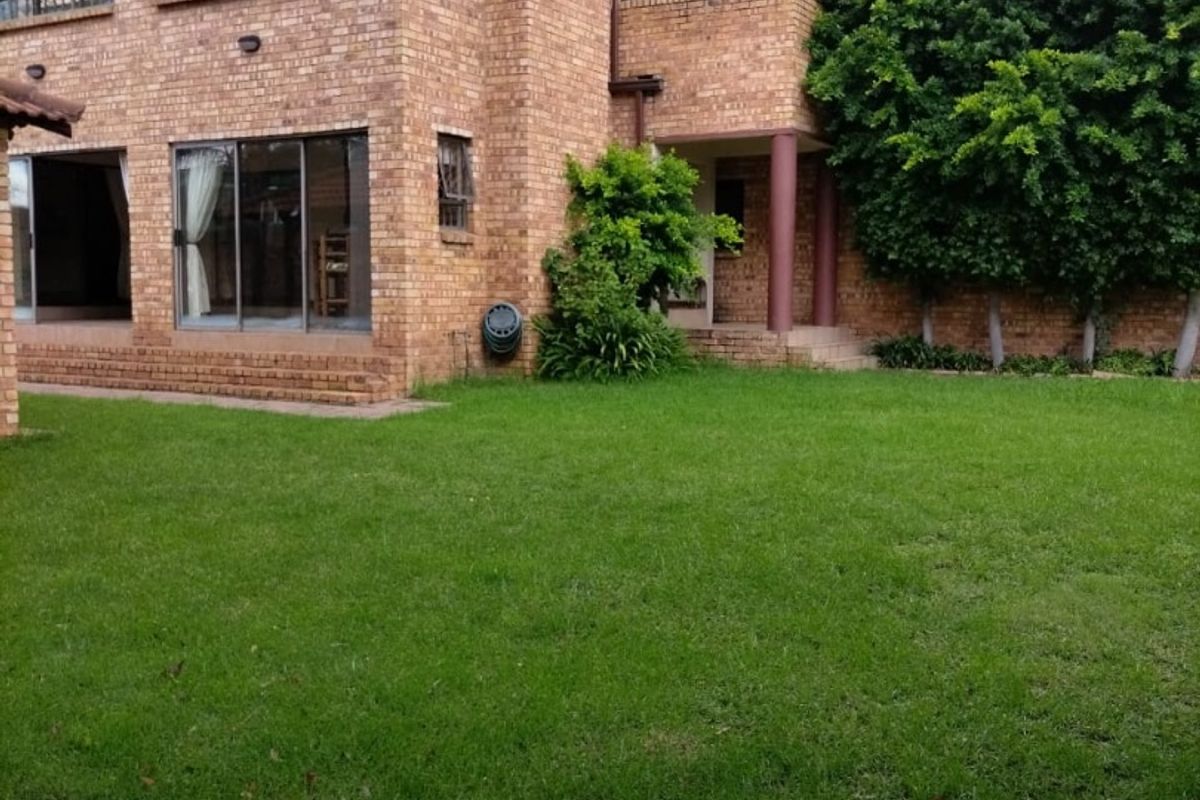 Rear view of a two-story face brick house featuring a large lawn, sliding glass doors, and an integrated chimney structure.