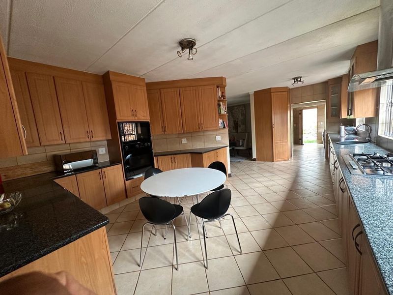 Spacious open-plan kitchen featuring extensive wooden cabinetry, granite countertops, built-in oven, and gas hob, with tiled flooring throughout.