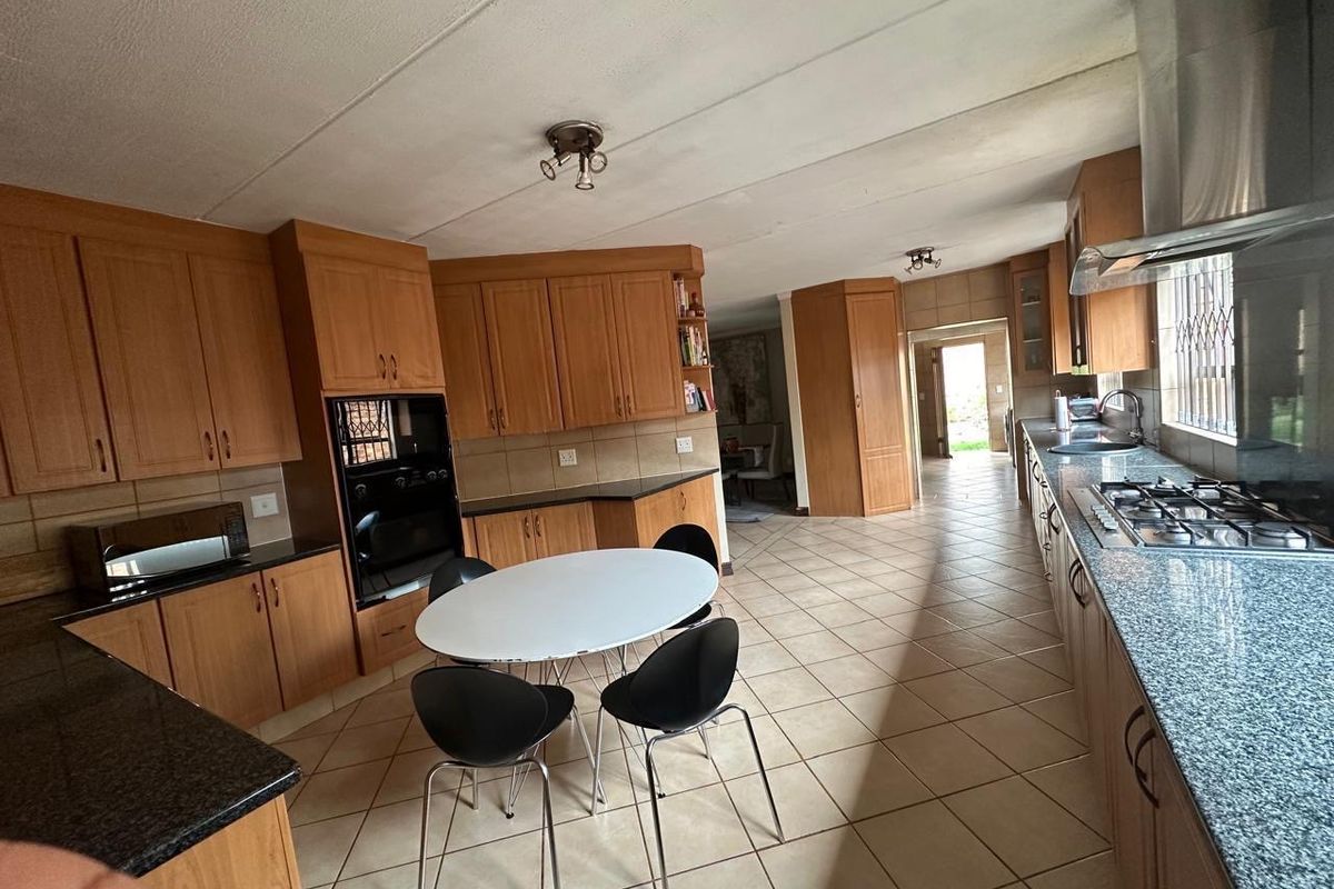 Spacious kitchen featuring extensive wooden cabinetry, granite countertops, gas hob, and integrated oven, with tiled flooring throughout and direct access to the living area.
