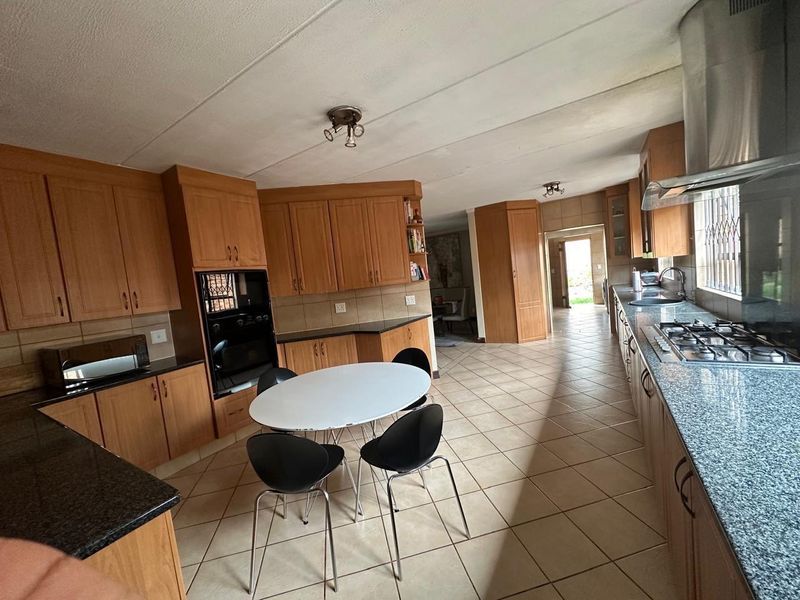 Spacious kitchen featuring extensive wooden cabinetry, granite countertops, gas hob, and integrated oven, with tiled flooring throughout and direct access to the living area.