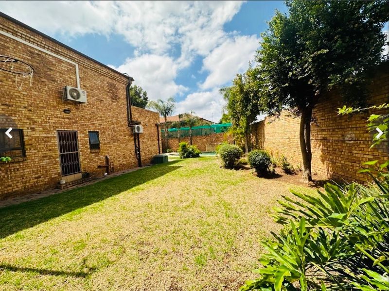 A spacious rear garden featuring a well-maintained lawn, perimeter brick walls, and exterior access to the main house structure.