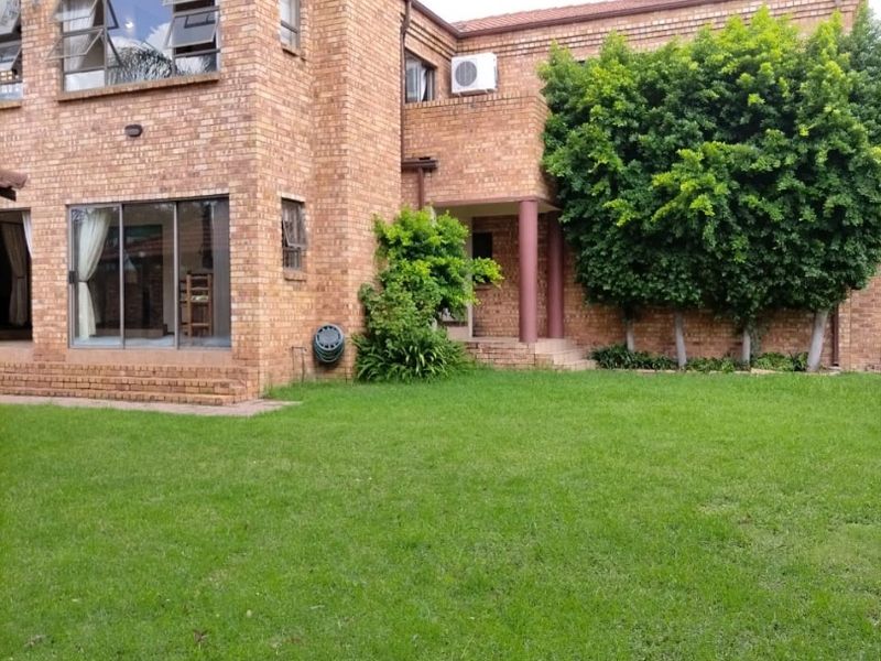 Rear view of a two-story face brick house featuring a large lawn, sliding glass doors, and an integrated chimney structure.