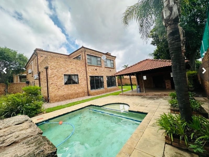 Rear exterior view featuring a facebrick house, a swimming pool, and a covered patio area in the garden.