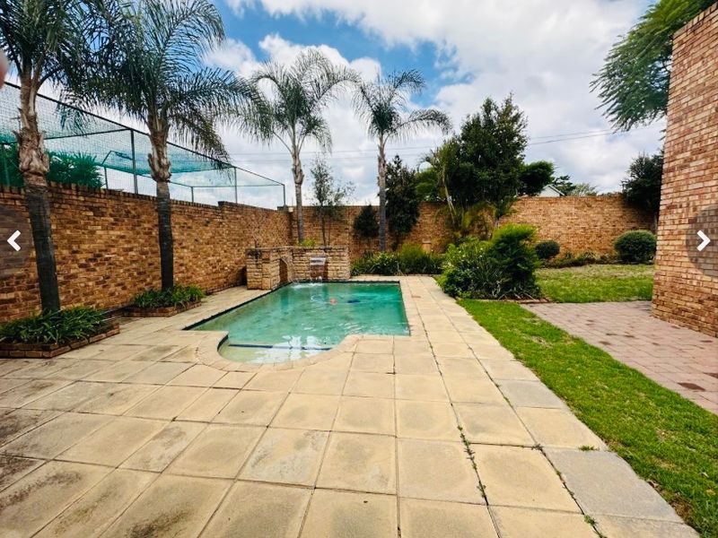Outdoor pool area featuring a swimming pool with a built-in water feature, surrounded by paved patio, lawn, and high brick boundary walls.